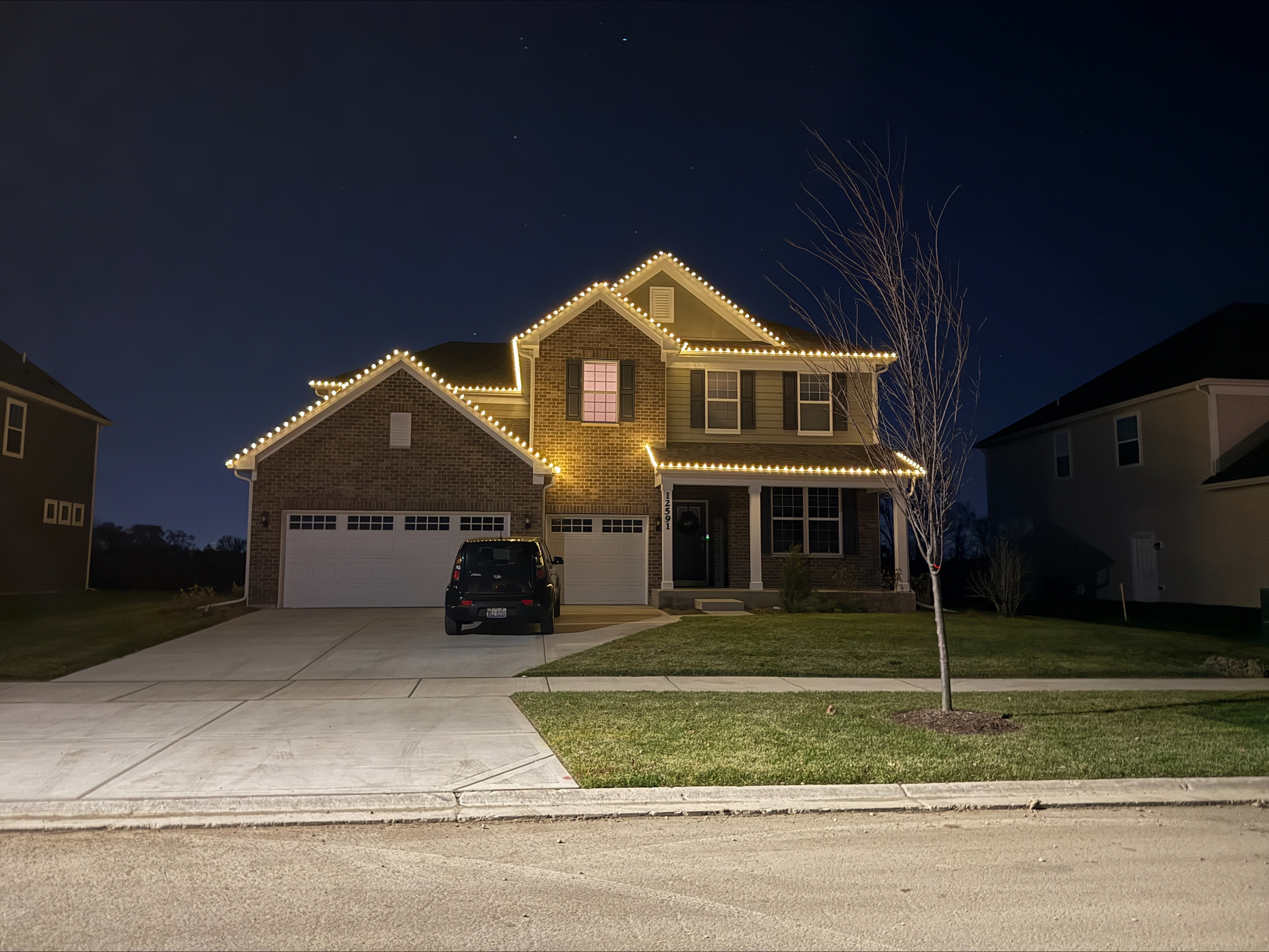 Two-story home with warm white C9-style Christmas lights outlining the roofline, garage, and gables